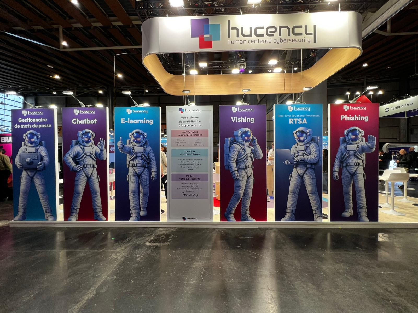 Forum InCyber Lille : Hucency présente Thomas, le RSSI virtuel qui co-pilote votre stratégie de cybersécurité. Stand Hucency au Forum InCyber de Lille. Sept panneaux colorés mettent en scène Thomas, le RSSI virtuel représenté en astronaute. Il illustre le co-pilotage de la stratégie cyber (phishing, e-learning, vishing) aux côtés des RSSI et DSI, sous une enseigne "human centered cybersecurity".